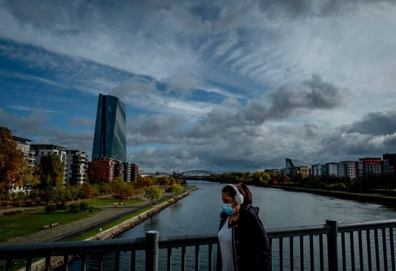 A woman wearing a face mask walks over a bridge with the European Central Bank at left in Frankfurt, Germany, Thursday, Oct. 29, 2020. (AP Photo/Michael Probst)