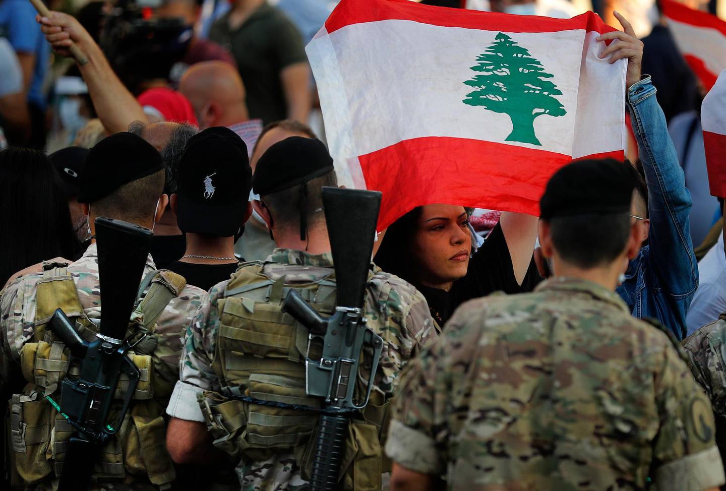 An anti-government protester holds a national flag, as she passes in front of Lebanese army soldiers during a protest against rising prices and worsening economic and financial conditions, in Zalka, north of Beirut, Lebanon, Monday, Oct. 5, 2020. Lebanon is passing through its worst economic and financial crisis in decades made worse by the coronavirus pandemic. (AP Photo/Hussein Malla)
