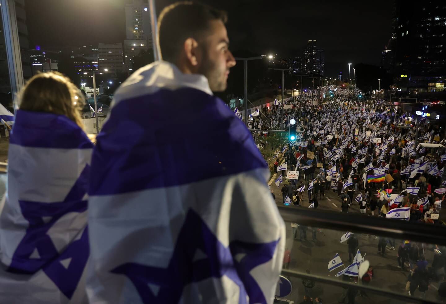 People wrapped in Israeli flags watch the Tel Aviv protest. EPA