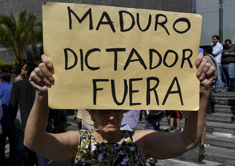 An anti-government activist holds a placard reading "Maduro Dictator Out" as the president of Venezuela's opposition-led National Assembly Juan Guaido speaks during an extraordinary open meeting in front of the headquarters of the United Nations Development Programme (UNDP) in Caracas on January 11, 2019. Venezuelan President Nicolas Maduro began a new term on Thursday, with the economy in ruins and his regime more isolated than ever as regional leaders declared his re-election illegitimate and shunned his inauguration. / AFP / Yuri CORTEZ
