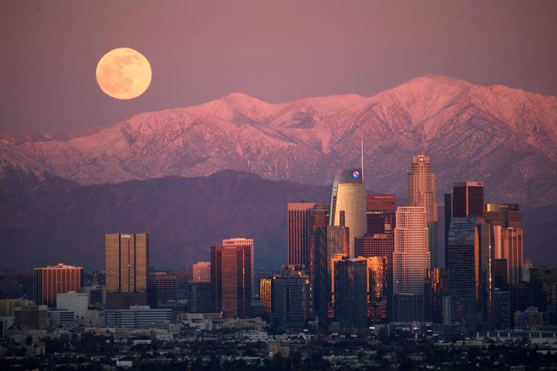 The last full moon of 2020, also known as the Cold Moon, rises behind the snow-topped San Gabriel Mountains and the Los Angeles downtown skyline at sunset as seen from the Kenneth Hahn State Recreation Area on December 29, 2020 in Los Angeles, California. (Photo by Patrick T. FALLON / AFP)