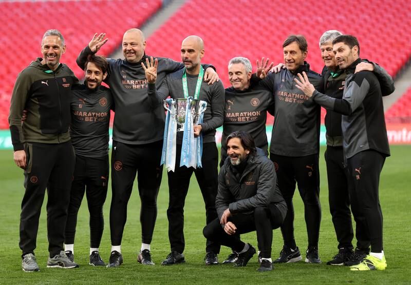 Pep Guardiola, manager of Manchester City, and his backroom staff celebrates with the trophy after winning the League Cup again in 2021. Getty