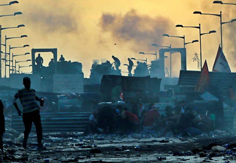 Anti-government protesters take cover while Iraqi security forces, back, fire tear gas and close the bridge leading to the Green Zone, during a demonstration at sunset in Baghdad, Iraq, Sunday, Oct. 27, 2019. Protests have resumed in Iraq after a wave of anti-government protests earlier this month were violently put down. (AP Photo/Khalid Mohammed)