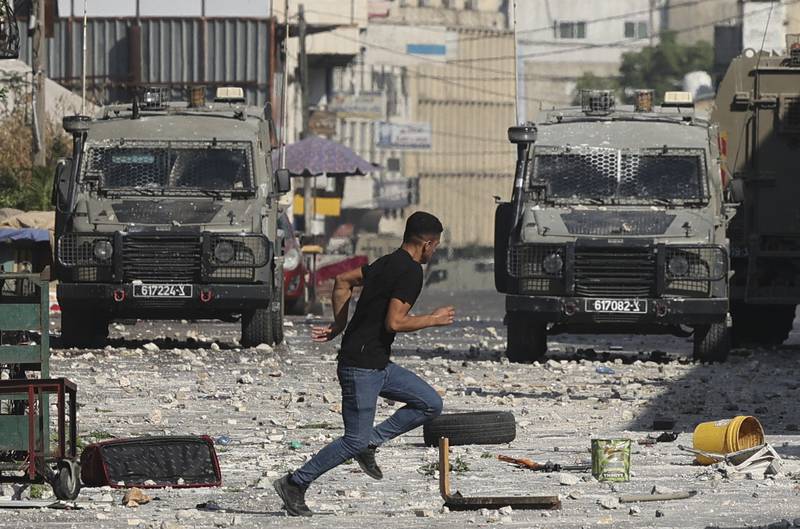 A Palestinian protester runs during clashes with Israeli security forces' vehicles. AFP