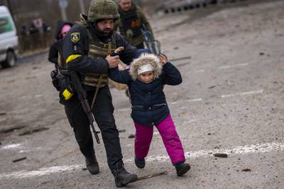 A Ukrainian police officer runs with a child as the sound of shelling echoes nearby in Irpin. AP
