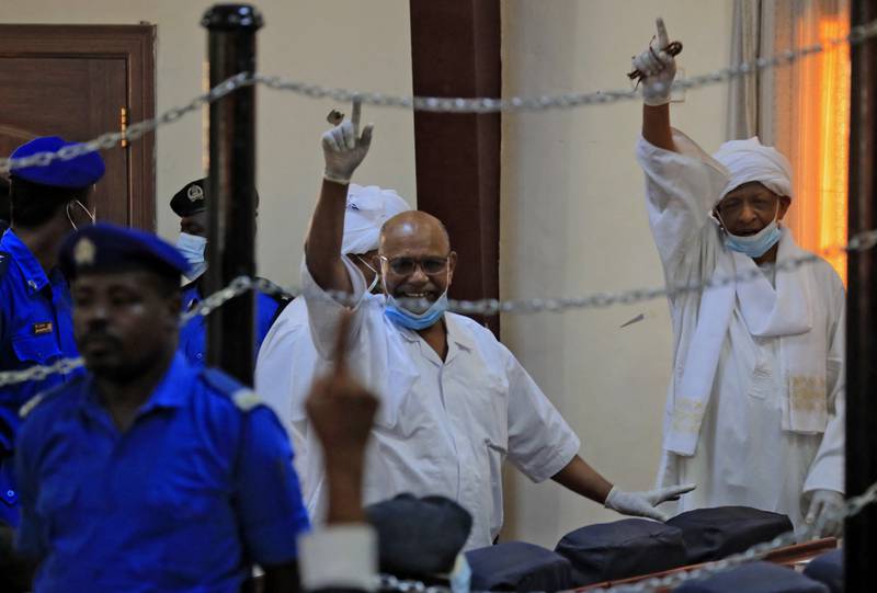 Sudan’s ousted president and his deputy, Nafeh Ali Nafeh, make gestures of defiance during their trial at a courthouse in Khartoum on January 19, 2021.