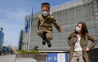 epa08363981 A mother and her son wearing face masks in front of European Commission headquarters during a press conference of European Council President Charles Michel and EU Commission President Ursula Von der Leyen on the Coronavirus pandemic in Brussels, Belgium, 15 April 2020.  EPA/OLIVIER HOSLET