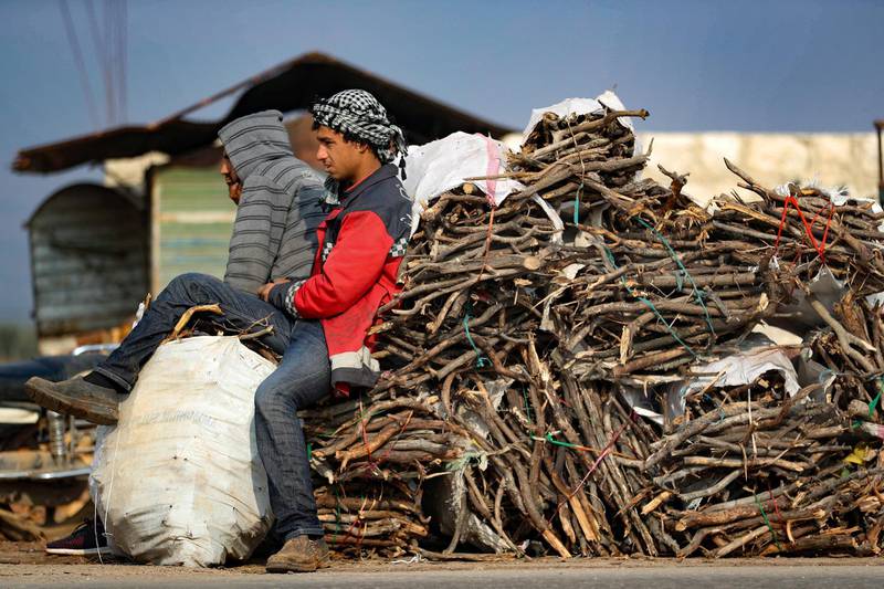 Displaced Syrians rest on a pile of wood logs destined to be sold to compatriots who fled conflict zones, to be used as a less expensive alternative to fuel for heating during the winter season, on the outskirts of the northwestern city of Idlib, on December 11, 2020. (Photo by OMAR HAJ KADOUR / AFP)