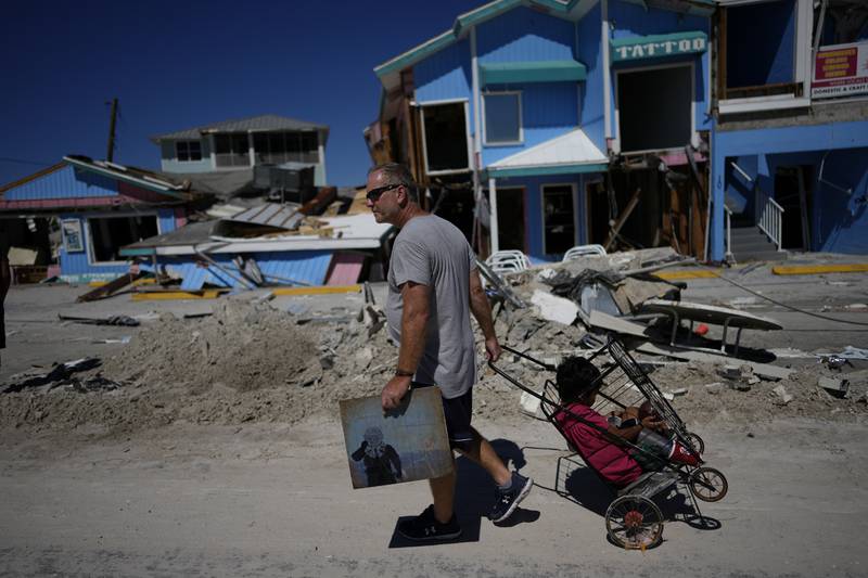Householder John Quigley carries a piece of artwork made by his daughter, the only item he found to salvage from the ruins of his home after Hurricane Ian, as he pulls his girlfriend's son Sebastian in a cart in Fort Myers Beach, Florida. AP