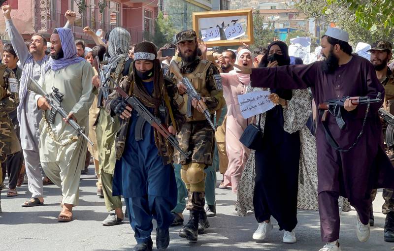 Taliban forces walk in front of Afghan demonstrators as they shout slogans during a protest, near the Pakistan embassy in Kabul. Academics warn that the Taliban could crack down on protests and commit genocide if financial aid is not restored. Reuters