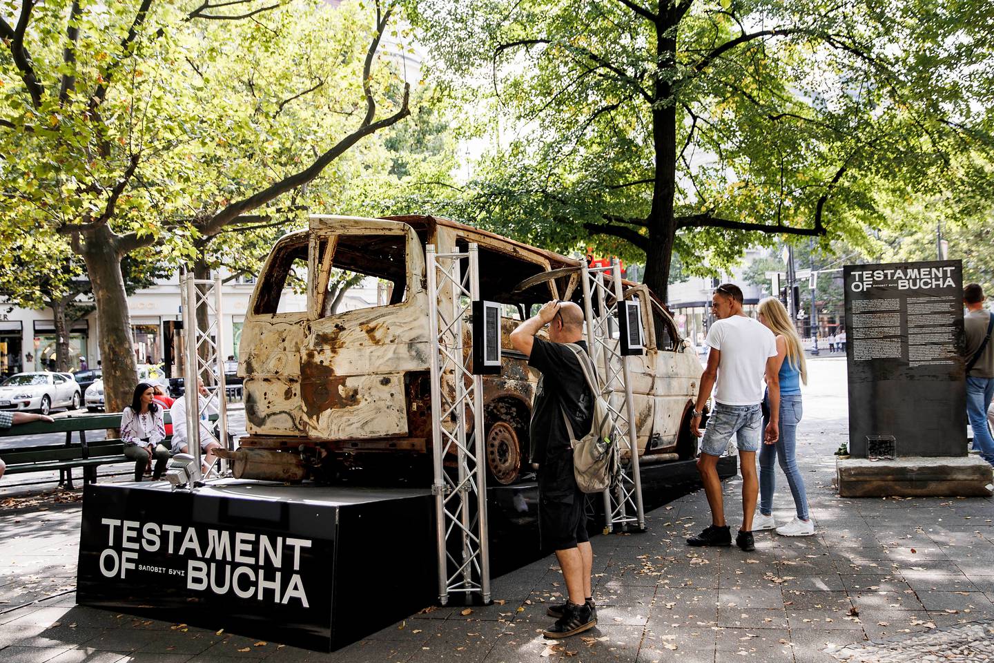 Passers-by in front of the "Testament of Bucha" exhibition in Berlin, on August 24, Ukraine's Independence Day and the six month mark since the beginning of the war. The wrecked car is one in which four fleeing Ukrainian women were shot at by the Russian military and died. Getty 