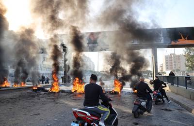 Lebanese men drive bikes past burning tyres set up by protesters to block a road in the capital Beirut on November 29. AFP
