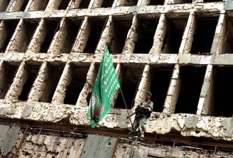 A Lebanese soldier stands in front of a building ravaged by the 1975-1990 civil war, alongside a flag for the Shiite Amal Movement.