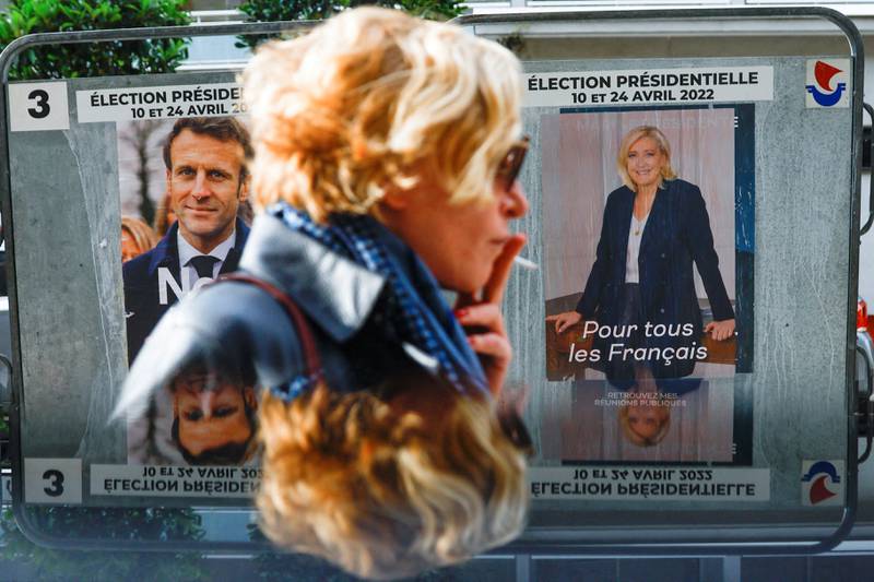 A woman walks past official campaign posters of French presidential election candidates Marine Le Pen, leader of the far-right National Rally (Rassemblement National) party, and President Emmanuel Macron, in Paris. Reuters