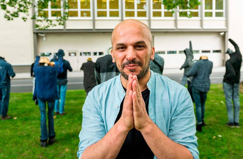 Syrian artist Khaled Barakeh poses in front of his installation titled "The Muted Demonstration" which consists of structures dressed in clothes that belong to Syrian activists currently residing in diaspora, on July 1, 2020 in Koblenz on the sidelines of a trial on state-sponsored torture in Syria. The artist goal is to shed light on the efforts of Syrians in their search for justice through an artwork that takes the form of a demonstration. The trial in Koblenz against two Syrian alleged former intelligence officers accused for crimes against humanity, is the first trial of its kind to emerge from the Syrian conflict. / AFP / Thomas LOHNES
