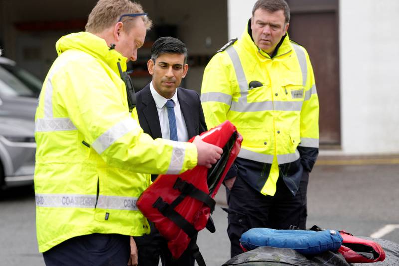 Mr Sunak speaks with Home Office staff while looking at a life vest and rubber dinghy. Reuters