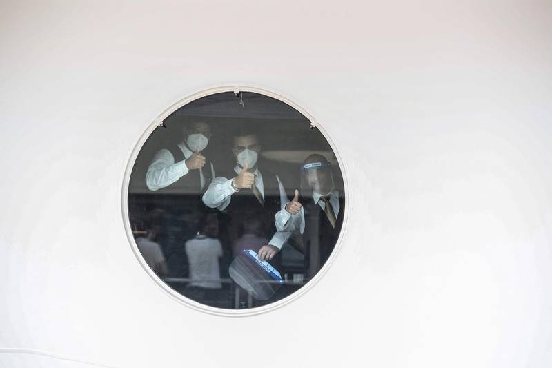 Staff of the 'MSC Grandiosa' cruise liner, seen through a porthole, give the thumbs-up. AFP