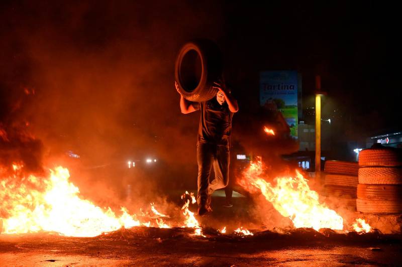 A protester throws a tyre on a fire lit by protesters to block the Dora highway in Beirut.  EPA