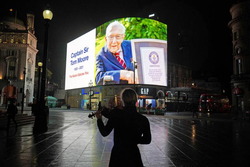 A woman plays the violin as a tribute to Captain Sir Tom Moore is displayed in Piccadilly Circus, London. The British Second World War veteran who entered the hearts of a nation in lockdown died after testing positive for Covid-19. He was 100.  AP