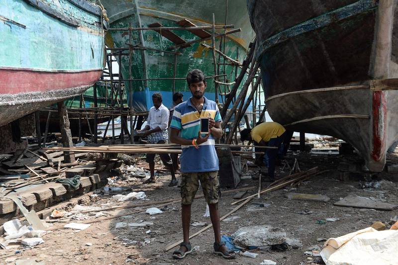 (FILES) In this file photo taken on November 9, 2018 Indian carpenter Deepan Raj, 25, poses with his smartphone at a fishing vessel dockyard at Kasimedu harbour in Chennai. / AFP / ARUN SANKAR
