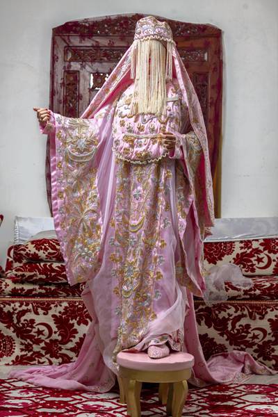 Madini outfit.This pink outfit is worn by the bride in Madinah region ( west of Saudi), it has many layers, especially on the face, kind of hiding the bride’s beauty till her groom sees her. A very interesting point about this, is that when the bride wears it, she marches down to the Kusha ( where she will sit- the stage) by stepping on two stools/ small chairs,  then the stool is moved again and she steps again kind of building a bridge till she reaches the Kusha ( the stage of the bride), which you will see me sitting on – pink cushions at the center. Hussain Haddad for The National. 