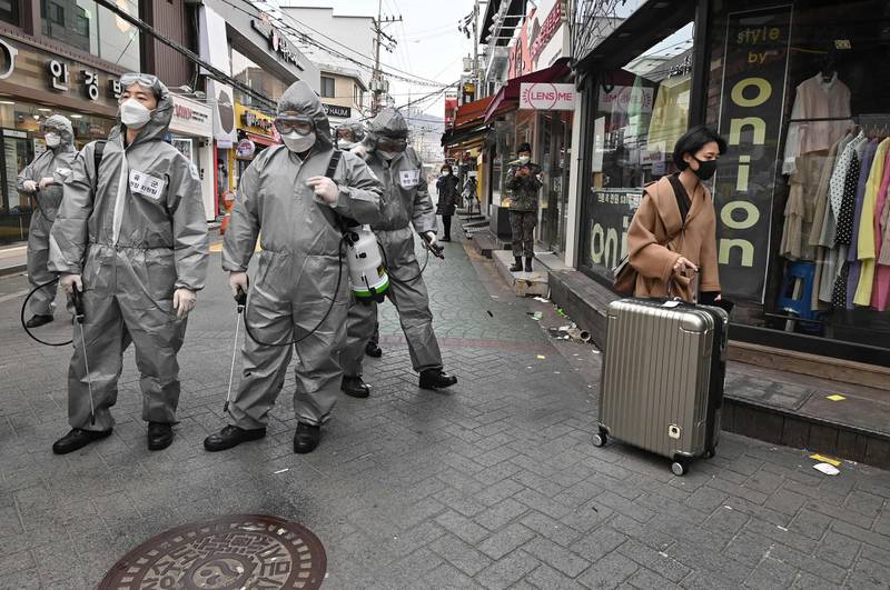A woman walks past South Korean soldiers wearing protective gear as they spray disinfectant to help prevent the spread of the COVID-19 coronavirus, at a shopping district in Seoul on March 4, 2020. South Korea reported 142 more novel coronavirus cases on March 4, a significantly lower increase than the day before, taking its total to 5,328 -- the largest in the world outside China. / AFP / Jung Yeon-je
