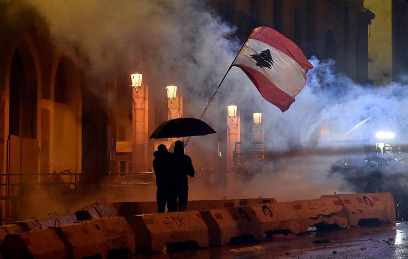 Two anti-government protesters wave a Lebanese national flag as they protect themselves with an umbrella during continuous protests and clashes with police outside the Lebanese Parliament building in downtown Beirut.  EPA