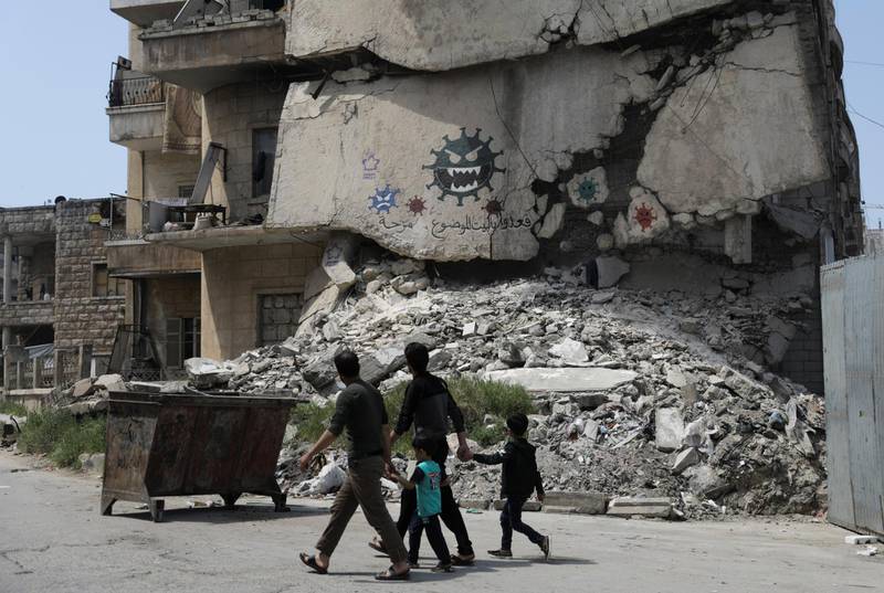 People walk past a damaged building depicting drawings alluding to the coronavirus and encouraging people to stay at home, in the rebel-held Idlib city, Syria. Reuters