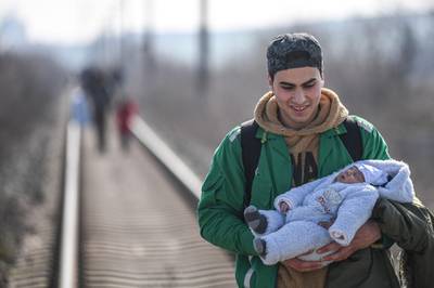 A migrant carries his baby as they walk on railways toward Meritsa river, near Edirne, to take a boat to attempt to enter Greece by crossing the river.  AFP
