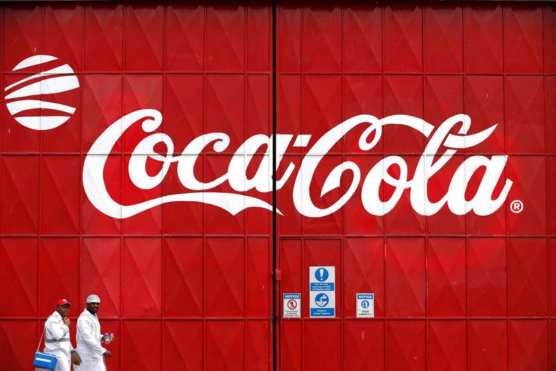 Workers walk past a Coca Cola logo painted on a gate at a Coca Cola factory in Nairobi, Kenya, June 7, 2018. REUTERS/Baz Ratner