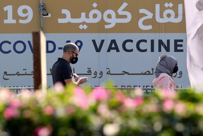 A man and a woman walk past a huge health ministry COVID-19 vaccines announcement outside a medical centre in Dubai on February 16, 2021, as the Gulf emirates goes ahead its vaccination effort. The UAE, home to a population of around 10 million, has administered some 4.6 million doses of vaccine, making it the second-fastest per capita delivery in the world, after Israel. / AFP / Karim SAHIB
