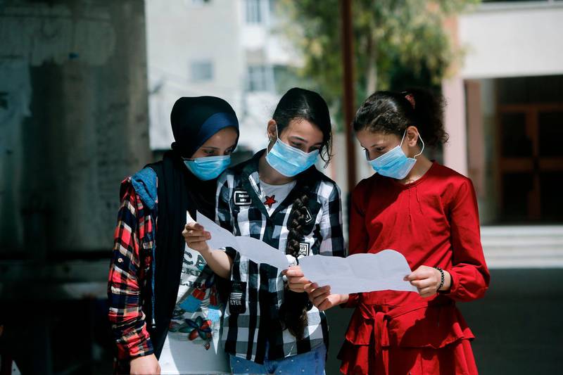 Palestinian school girls wearing face masks due to the COVID-19 coronavirus pandemic view their end of year certificates upon receiving them at a school in Gaza City.   AFP