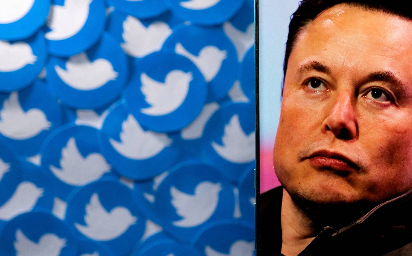 An image of Elon Musk is seen on a smartphone placed on printed Twitter logos. Reuters