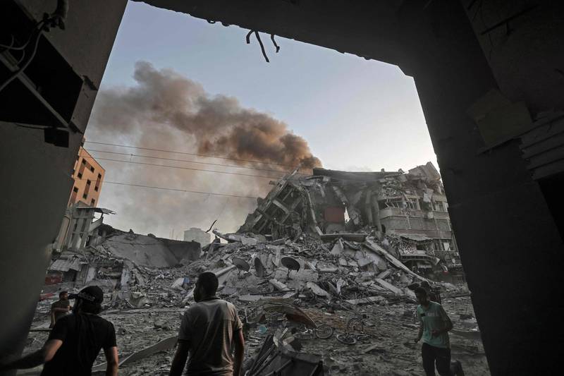 People gather amidst the rubble in front of Al-Sharouk tower that collapses after being hit by an Israeli air strike, in Gaza City, on May 12, 2021. An Israeli air strike destroyed a multi-storey building in Gaza City today, AFP reporters said, as the Jewish state continued its heavy bombardment of the Palestinian enclave. AFP