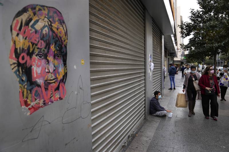 Shoppers pass a masks street vendor sitting on the ground next to a shop that has closed amid the country's economic crisis.