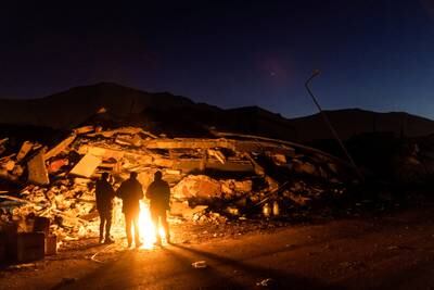 People stand by the fire next to the ruins of a collapsed building in Elbistan, Turkey. Reuters