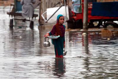 A girl carries a tea kettle as she wades through a flooded street after heavy monsoon rains in Pakistan's port city of Karachi.   AFP