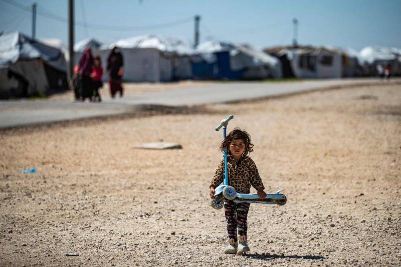 A child carries a scooter along a dirt road at Camp Roj. White tents – visible in the distance – are used to shelter families. AFP
