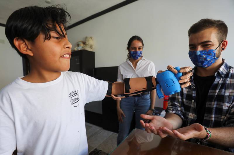 Moyolema, 8, who was born missing the lower part of his left arm, picks a toy up using a 3D-printed prosthetic with Martinez, founder of Madrid-base social entity Ayudame3D in Spain, looking on. Reuters