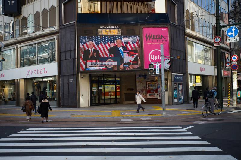 Pedestrians walk past a digital screen displaying a news report on the U.S. presidential election in Sapporo, Hokkaido, Japan. Bloomberg