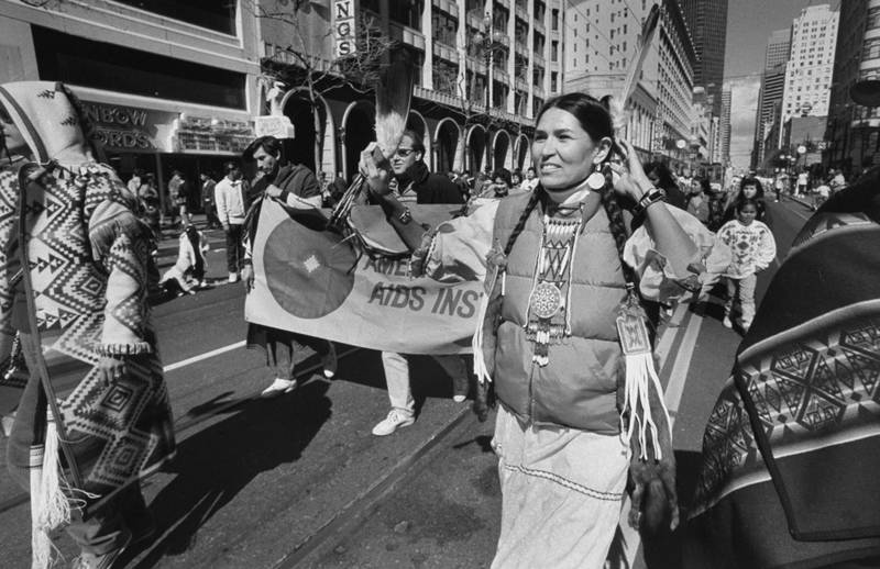 Littlefeather adorned with tribal, beaded pigtail decorations and a feather in her hair as she wears a down jacket over a squaw dress while marching in a street parade in San Francisco. Getty Images
