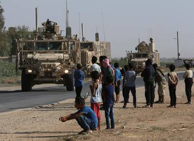 Syrians watch a US armoured convoy pass on a road to Raqqa.