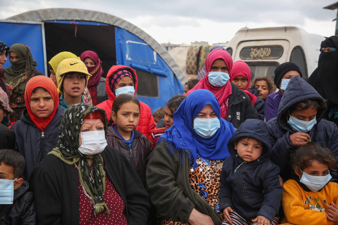 Displaced Syrian, some wearing protective masks, listen as medics hold an awareness campaign on how to be protected against the novel coronavirus pandemic, in a camp for displaced people in Kafr Lusin, in the northwestern province of Idlib, following heavy storms on March 18, 2020.   / AFP / Mohammed AL-RIFAI
