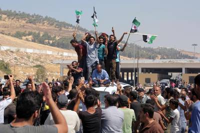 Protesters chant slogans as they hold Syrian revolutionary flags during a demonstration at the Bab al-Hawa border crossing with Turkey, Syria, Friday, Aug. 30, 2019, demanding that Ankara either open the border or end attacks by the government. Opposition activists said Turkish borders guards fired tear gas at the protesters. (AP Photo)