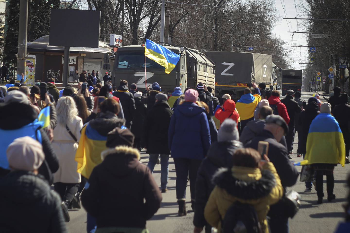 Des personnes portant des drapeaux ukrainiens marchent vers des camions de l'armée russe lors d'un rassemblement contre l'occupation russe à Kherson, en Ukraine.  PA