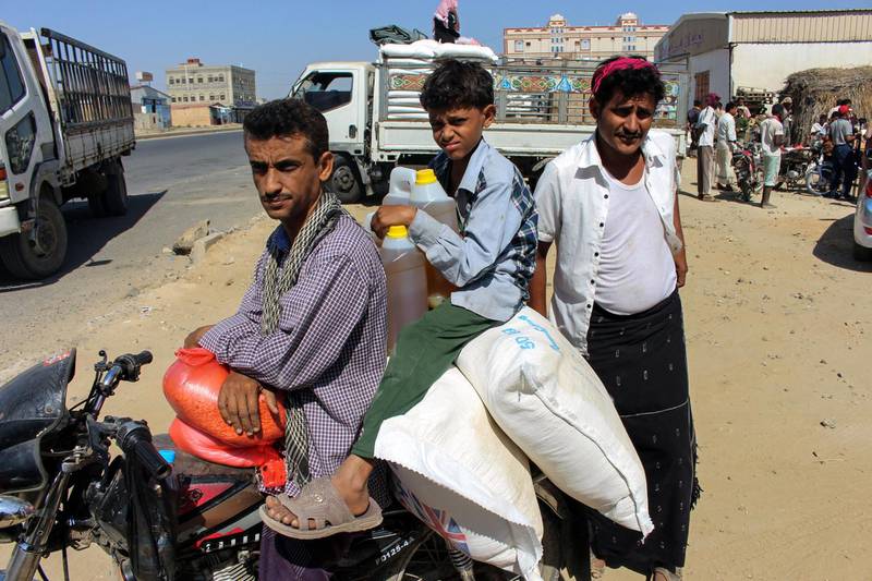 A Yemeni man and child ride on a motorcycle loaded with sacks of wheat and cooking oil containers distributed as food aid by a local charity at a camp for the displaced, in the northern province of Hajjah on December 23, 2017. / AFP PHOTO / STRINGER
