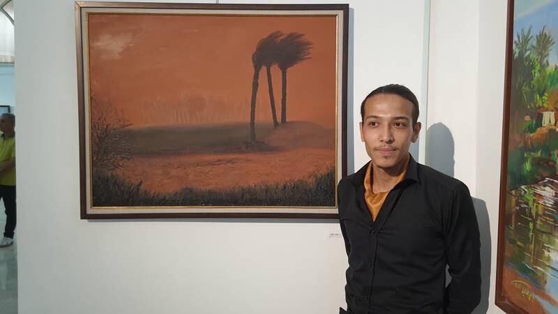 Artist Masoud Al Jameel stands next to his painting that depicts the scene of a heavy sandstorm that turns the sky of an arid agricultural area to reddish-brown. All photos: Sinan Mahmoud / The National
