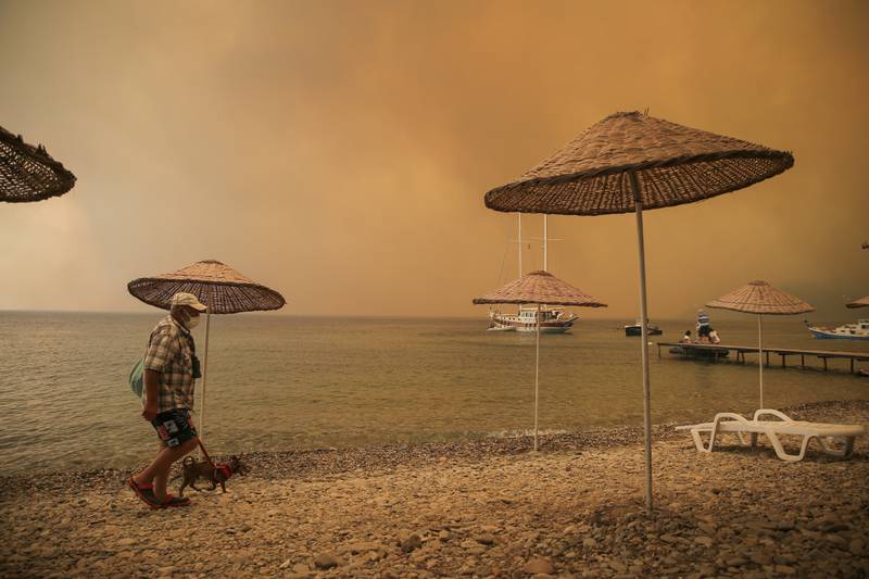 A man walks with his dog on the beach of smoke-engulfed Mazi area as wildfires rolled down the hill toward the seashore, in Bodrum, Mugla.