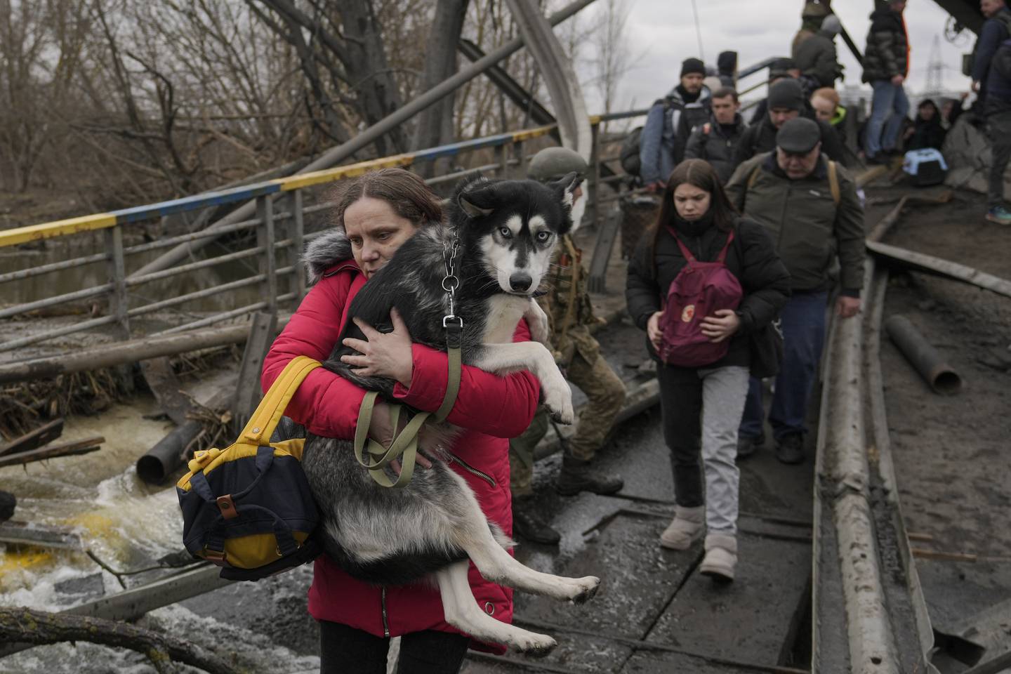 A woman holds a dog while crossing the Irpin River on an improvised path under a bridge as people flee the town of Irpin, Ukraine.  AP