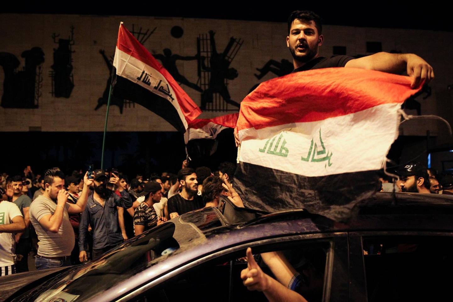 Iraqi protestors wave Iraq's national flags frome a car;s sun-roof as they take part in anti-government demonstrations in Baghdad's Tahrir Square on October 24, 2019. Anti-government rallies renewed across Iraq late on October 24, 2019, the second phase of protests denouncing corruption and unemployment before evolving into calls for an overhaul of the political system that turned deadly earlier this month and which could balloon after the endorsement of populist cleric Moqtada al-Sadr. / AFP / -
